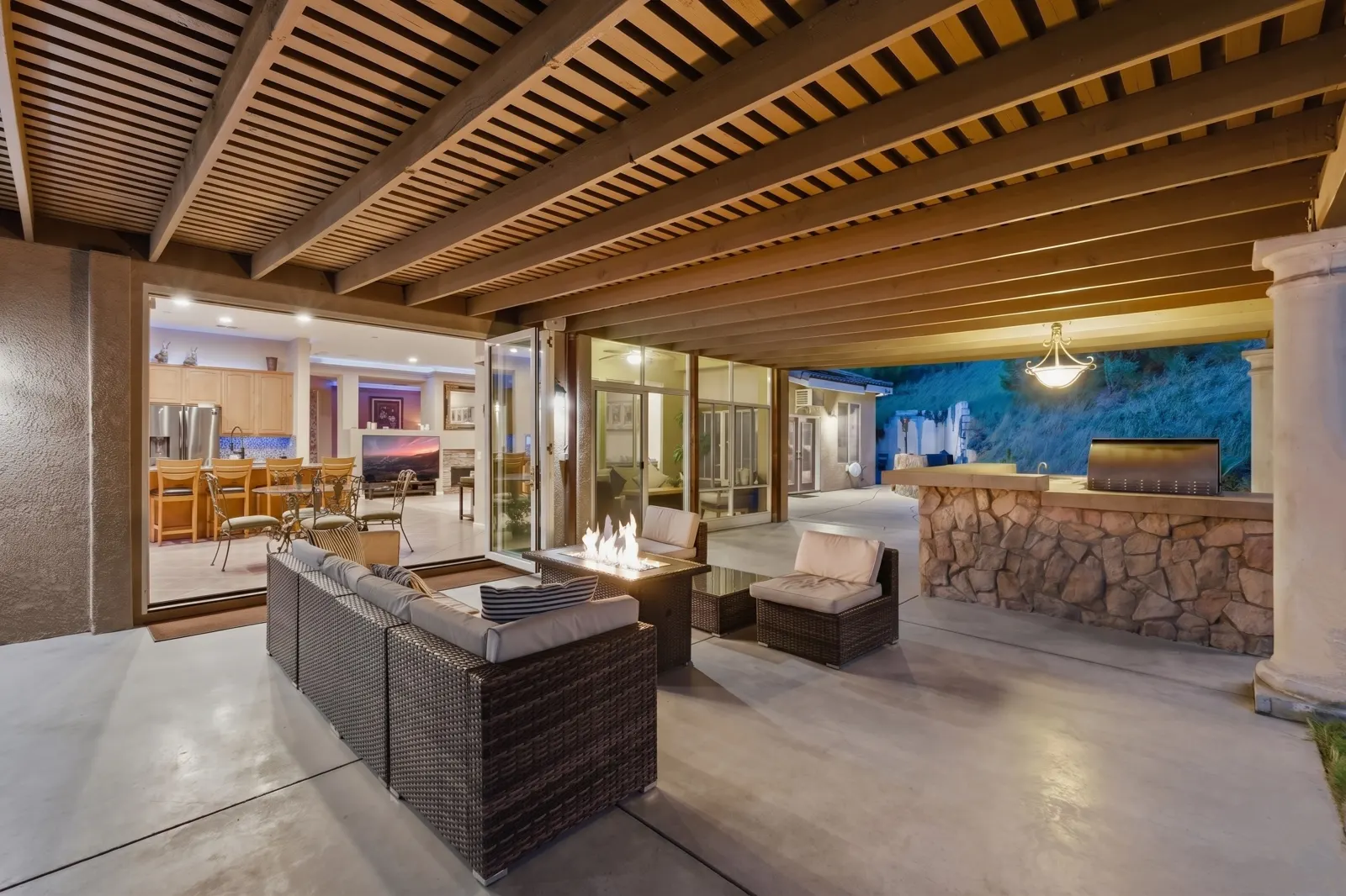 Covered patio with fire pit and outdoor kitchen at twilight